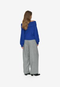 Blå off-shoulder tröja med ribbat halslinning, kombinerad med grå vida byxor och svarta klackskor. Slät tyg och avslappnad passform.