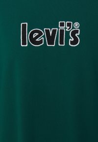 Green cotton t-shirt featuring a prominent embroidered black "levi's" logo on the front. Smooth texture and short sleeves.