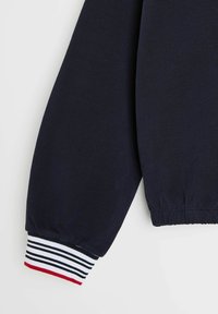 Morska niebieska bluza z długim rękawem, zakończona ściągaczem, zdobiona poziomymi paskami w kolorze białym, morskim i czerwonym. Miękka, oddychająca struktura materiału.