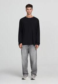 Czarna koszulka z długim rękawem i okrągłym dekoltem, połączona z jasnoszarymi dżinsami. Obuwie utrzymane w neutralnej kolorystyce z akcentami.