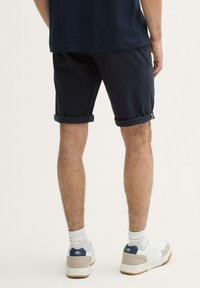 Pantaloni scurți din bumbac de culoare bleumarin cu mansete răsucite, având o textură netedă. Asortați cu adidași albi și șosete până la gleznă. Design simplu și contemporan.