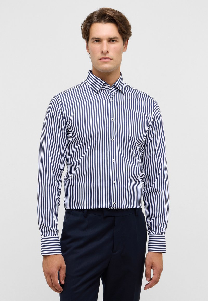Marineblau-weiß gestreiftes Langarmhemd mit Button-Down-Kragen, taillierte Passform, glatte Textur, kombiniert mit dunkler Hose.