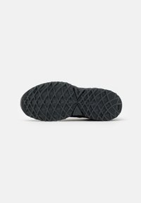 Sole di scarpa sportiva nera con una superficie in gomma testurizzata caratterizzata da un motivo geometrico di linee incrociate e profondità variabili per una migliore trazione.
