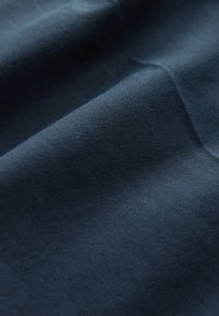 Tissu bleu marine à texture lisse, présentant des plis subtils et un motif de tissage fin et régulier, indiquant une élasticité et une douceur.