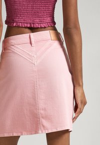 Mini falda de mezclilla rosa con una cintura ajustada, costuras visibles y una etiqueta de cuero. Presenta un ligero vuelo y un diseño de costura trasera único.