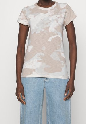 Personne portant un t-shirt à manches courtes à motif abstrait beige et blanc, associé à un jean taille haute bleu clair.
