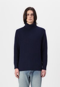 Marineblauer, gerippter Strickpullover mit hohem Rollkragen und langen Ärmeln. Das Design zeichnet sich durch eine entspannte Passform und eine strukturierte Oberfläche aus. Kombiniert mit hellen Jeans.
