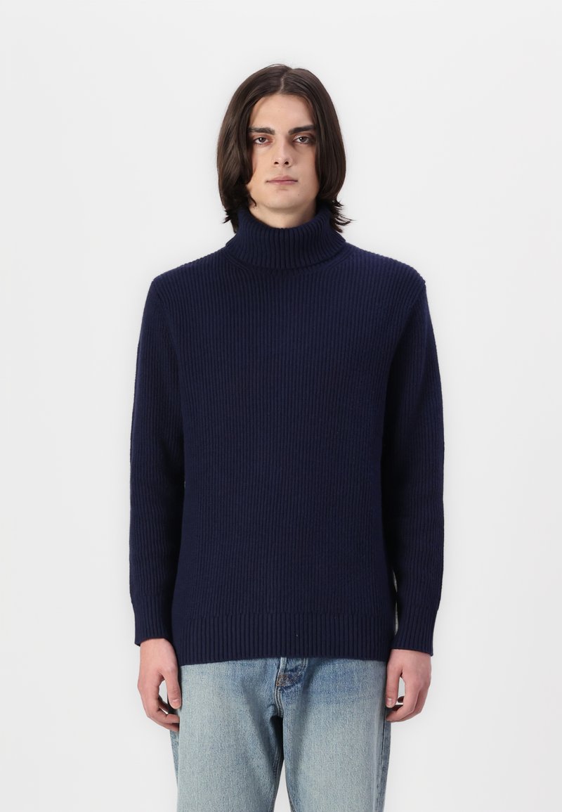Marineblauer, gerippter Strickpullover mit hohem Rollkragen und langen Ärmeln. Das Design zeichnet sich durch eine entspannte Passform und eine strukturierte Oberfläche aus. Kombiniert mit hellen Jeans.
