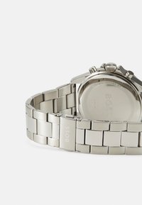Montre en acier inoxydable argenté avec une finition polie, bracelet à maillons et un fond de boîtier circulaire. Caractéristiques d'un logo gravé et d'une indication de résistance à l'eau.