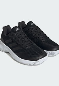 Scarpe da atletica nere con tomaia in rete, suola in gomma bianca e lacci neri. Presentano tre strisce nere sui lati e accenti di marca.