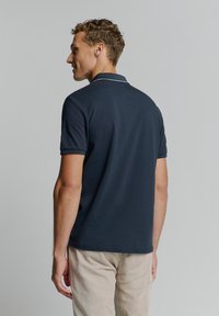 Marineblauwe polo met een effen kleurontwerp en een contrasterende donkergroene kraag. Korte mouwen, zachte stof en een reguliere pasvorm.