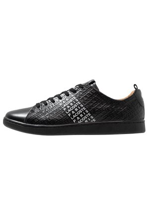 Baskets basses noires avec texte en relief répétant "Lacoste Paris" sur les côtés et lacets noirs.