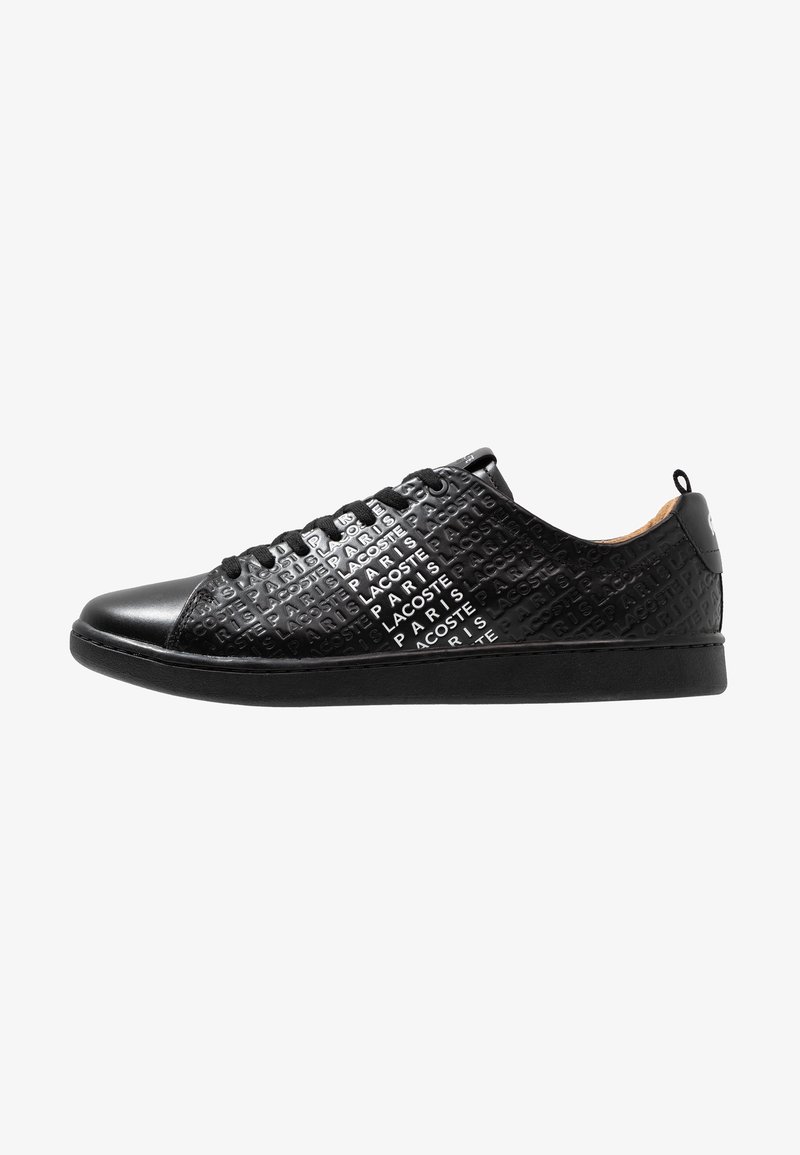 Baskets basses noires avec texte en relief répétant "Lacoste Paris" sur les côtés et lacets noirs.
