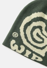 Căciulă verde cu un design contrastant în spirale albe și un logo. Textură tricotată, formă rotundă și se potrivește strâns.