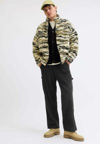 Pahuljasti bež kaput s crnim i maslinastim prugama, složen preko crnog kardigana i bijele košulje. Uparen s tamnim hlačama i smešnim cipelama.