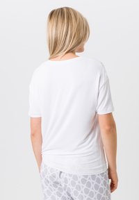 Wit T-shirt met korte mouwen en ronde hals, gemaakt van lichte stof en met een ontspannen pasvorm, gecombineerd met grijze pyjamabroek met een patroon.