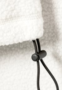 Tela de forro blanco con una superficie texturizada, que presenta un cordón negro y un cierre tipo toggle en el dobladillo para un ajuste ajustable.