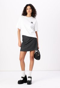 White oversized t-shirt with black graphic, charcoal gray mini skirt, black platform shoes, white ankle socks, and a black handbag.