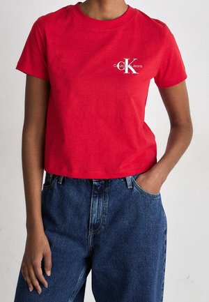 Czerwona bawełniana koszulka z krótkim rękawem i okrągłym dekoltem z białym logo Calvin Klein Jeans. W zestawie z wysokim stanem niebieskimi dżinsami.