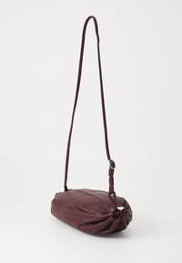 Borsa a spalla in pelle bordeaux con una forma morbida e arrotondata, dettaglio annodato a un'estremità e tracolla regolabile. Texture liscia in tutto il suo corpo.