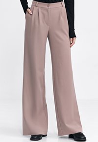 Jasnoróżowe spodnie o szerokich nogawkach o gładkiej fakturze, z zapięciem na guzik i pliskami. W połączeniu z czarnym obuwiem.