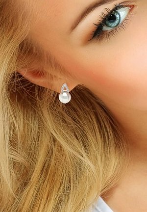 Boucles d'oreilles en forme de goutte avec une perle au centre, entourée de cristaux transparents, montées en métal argenté. Elles présentent une finition polie et une texture lisse.