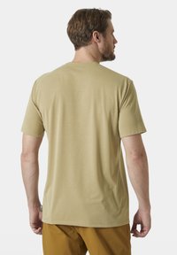 Beige tričko s krátkým rukávem z hladkého materiálu, s kulatým výstřihem a rovnými lemy, nošené s hořčicově žlutými kalhotami. Bez viditelných log.