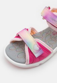 Roza otroška sandal s trakovi v mavričnem prehodu, mrežnim materialom in sivim vložkom s krožnim vzorcem. Bela gumijasta podplat.