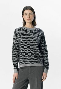 Schwarzer und grauer strickpullover mit Rautenmuster, langen Ärmeln und rundem Ausschnitt, kombiniert mit grauen Hosen.