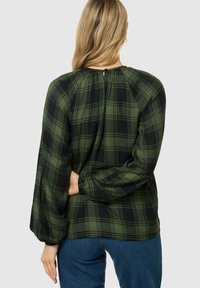 Grüne und schwarze Karobluse mit langen, gerafften Ärmeln, hohem Kragen mit Knopfverschluss und Rückenschlitzdetails. Weicher Stoff.