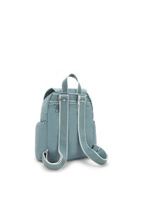 Ryggsäck i mjuk, dämpad blå tyg; har justerbara remmar, sidofickor och silverdetaljer med vita accenter. Minimalistisk design.