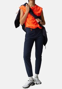 Haut orange sans manches, pantalon ajusté bleu marine avec cordon de serrage, et baskets noires et blanches. Design minimaliste, textures lisses.