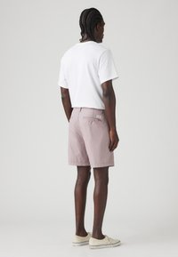 Tricou alb din bumbac și șorturi ușor roz cu buzunar pe spate. Încălțăminte sport de culoare crem cu accente negre. Textură netedă, design casual.