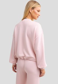 Sudadera rosa de manga larga con un corte relajado, dobladillo elástico y textura suave. Cuenta con hombros caídos y un cuello redondo.