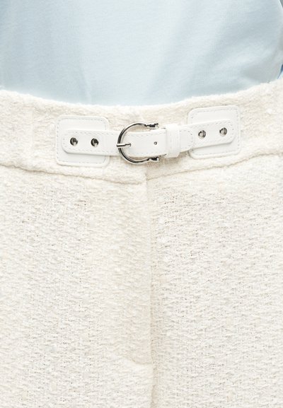 Λευκό υφασμάτινο παντελόνι με λευκή ζώνη που διαθέτει ασημένια κυκλική αγκράφα, φορεμένο πάνω σε ανοιχτό γαλάζιο τοπ.