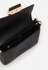 Musta tekstuuriga nahk-kott kuldse metallluku klambriga. Siseosa sisaldab ühte lukuga taskut ja ühte libistatavat taskut organiseerimiseks.