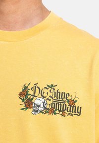 Geel katoenen t-shirt met een grafisch ontwerp van een schedel en rozen, vergezeld van de tekst "DC Shoe Company 1994" in het zwart.