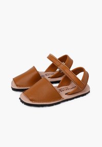 Sandali in pelle beige con punta aperta, cinturino regolabile e suola in gomma nera texturizzata. Presentano cuciture visibili lungo i bordi.