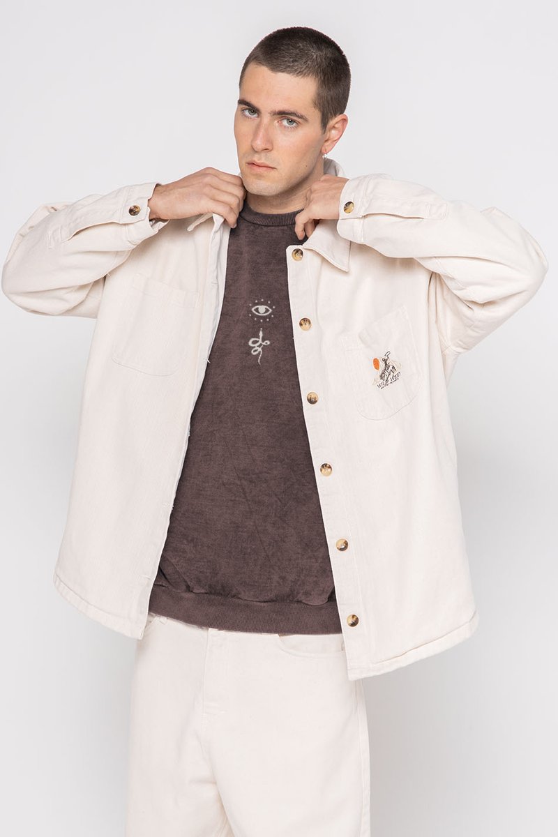 Crème-kleurige kanvas overhemdjacket met messing knopen, voorzien van twee borstzakken en een geborduurd ontwerp op de linkerzak.