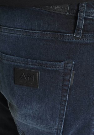 Jeans in denim blu scuro caratterizzati da una finitura testurizzata, una tasca posteriore con un'etichetta in pelle nera e cuciture dettagliate lungo le cuciture.