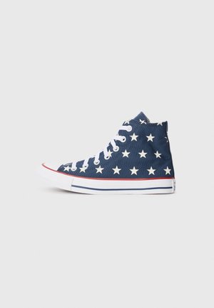 Zapatilla deportiva de lona azul marino de caña alta con estrellas blancas, cordones blancos, franja roja sobre suela de goma blanca y línea azul en el borde de la suela.