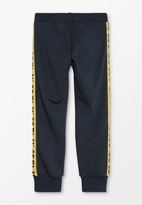 Marina joggerbyxor i mjukt tyg, med gula sidostråk med bokstäver, elastisk midja och avsmalnande fållar.