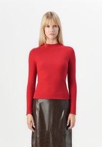 Rød ribbet langermet topp med en tettsittende design, båtutringning og rå kant. Kombinert med et brunt skinnskjørt med glatt tekstur.