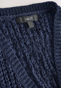 Cardigan en maille bleu marine avec un tissage lâche et texturé. Dispose d'un col côtelé et d'une étiquette "NEXT" à l'arrière.