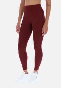 Leggings burdeos de cintura alta hechos de material elástico, diseñados para la comodidad y el movimiento, combinados con zapatillas deportivas blancas.
