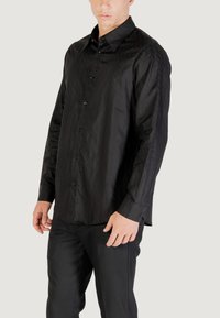 Camicia nera con bottoni caratterizzata da un motivo trapuntato, maniche lunghe e colletto. Realizzata in un tessuto leggero e liscio.