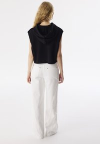 Czarna bezrękawnikowa, skrócona bluzka z kapturem, w połączeniu z białymi spodniami z szerokimi nogawkami, z postrzępionymi bocznymi szwami i tylnymi kieszeniami.