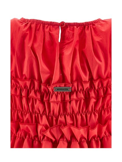 Tissu rouge froncé avec des volants, un seul bouton rouge en haut, et une étiquette de marque Monnalisa argentée cousue au centre.