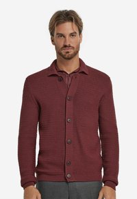 Burgunderfärgad stickad cardigan med ett texturerat mönster, ribbade ärmslut och nederkant, samt fem mörka knappar fram. Kragdesign.