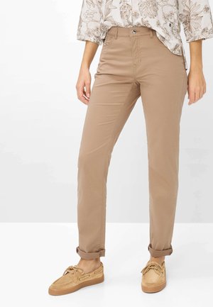 Beige, tætsiddende bukser rullet op ved anklerne, kombineret med tanfarvede bådsko med snørebånd og en bluse med blomsterprint og opklemte ærmer.